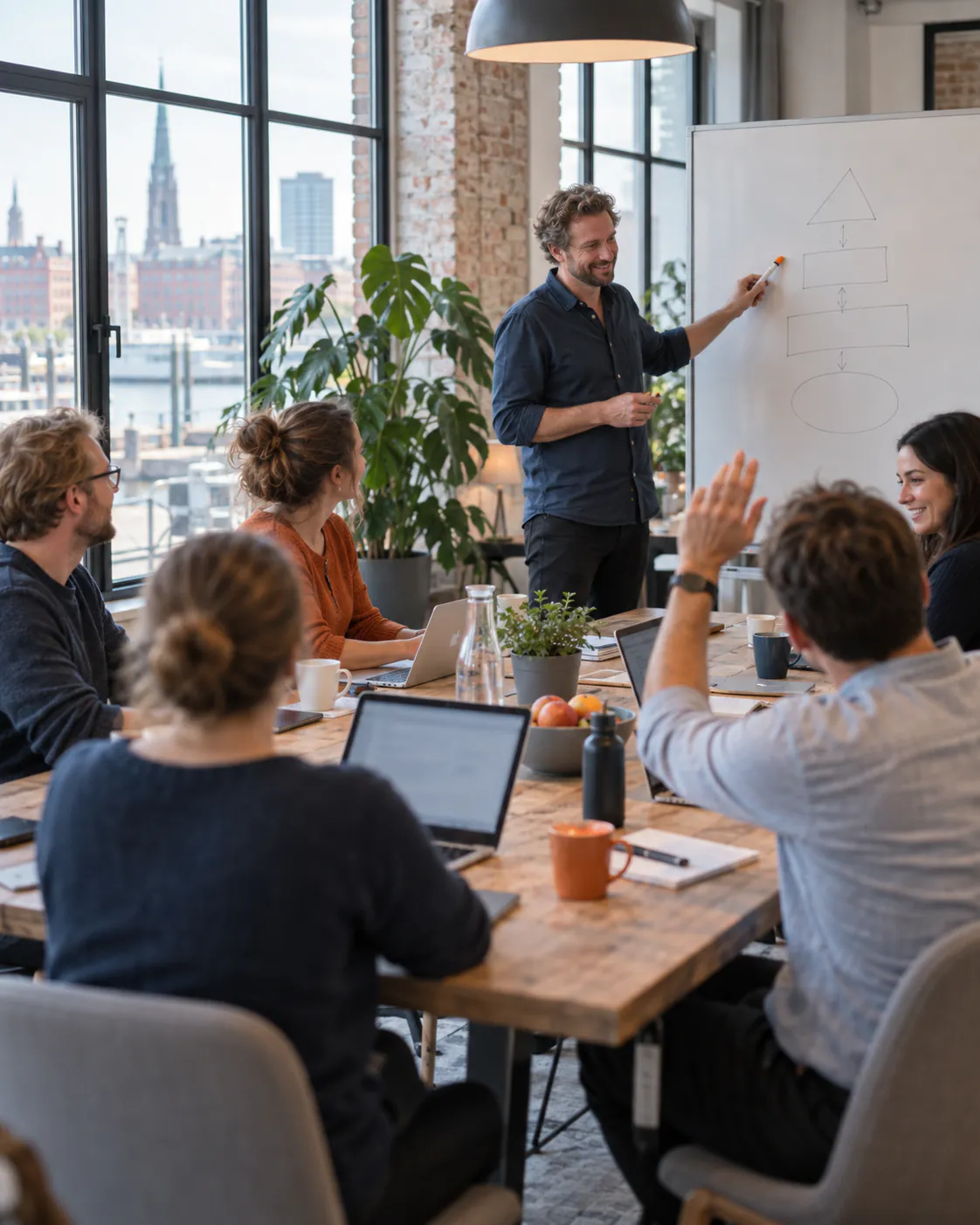 Lockere Trainingsrunde an einem großen Tisch, ein Trainer erklärt am Whiteboard